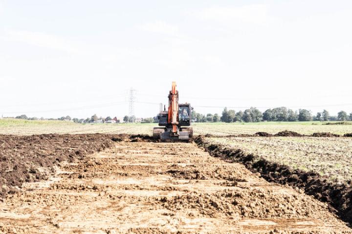 Foto van een kraan die bezig is met het omkeren van de toplaag, de zandlaag en de veenlaag